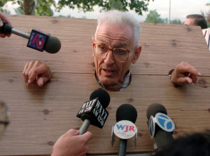 Dr. Jack Kevorkian meets the press in homemade stocks before his arraignment on assisted suicide charges at the Oakland County courthouse in Pontiac, Mich., Thursday, Sept. 14, 1995. Kevorkian, a retired pathologist who advocates doctors helping the terminally ill who wish to commit suicide, was wearing the laminated cardboard stocks in apparent reference to a state Supreme Court ruling that said assisted suicide could be prosecuted in Michigan under common law. (AP Photo/Carlos Osorio)